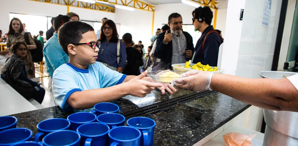 Seorang anak berkacamata menerima piring berisi makanan.