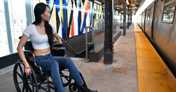 Seorang perempuan disabilitas mendorong kursi roda di peron kereta.