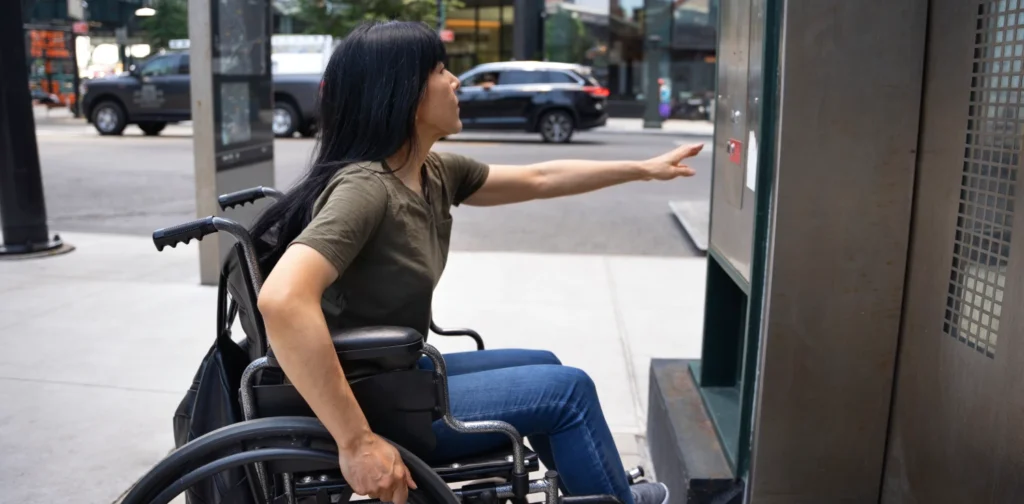 Seorang perempuan pengguna kursi roda sedang meraih tombol lift.