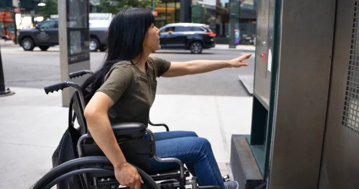 Seorang perempuan pengguna kursi roda sedang meraih tombol lift.