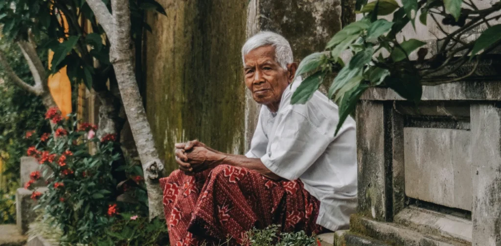 seorang pria tua duduk sendiri di dekat tembok dan tanaman