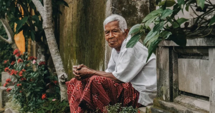 seorang pria tua duduk sendiri di dekat tembok dan tanaman