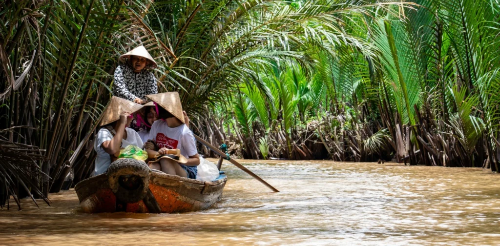 Sekelompok orang menaiki perahu di sungai Mekong yang dikelilingi pepohonan