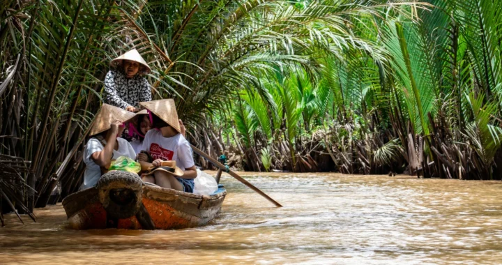 Sekelompok orang menaiki perahu di sungai Mekong yang dikelilingi pepohonan