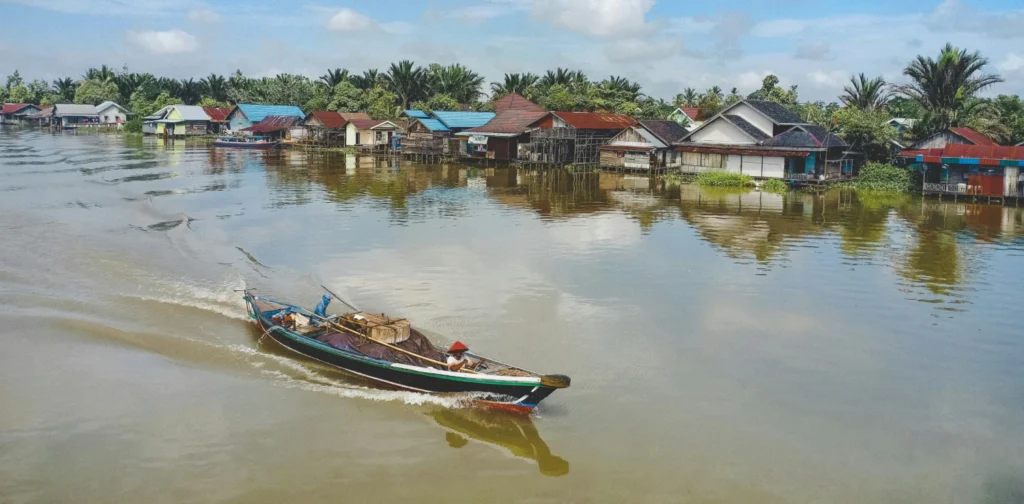 Sebuah kapal nelayan yang sedang melaju di sungai dekat perkampungan.