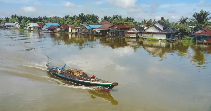 Sebuah kapal nelayan yang sedang melaju di sungai dekat perkampungan.