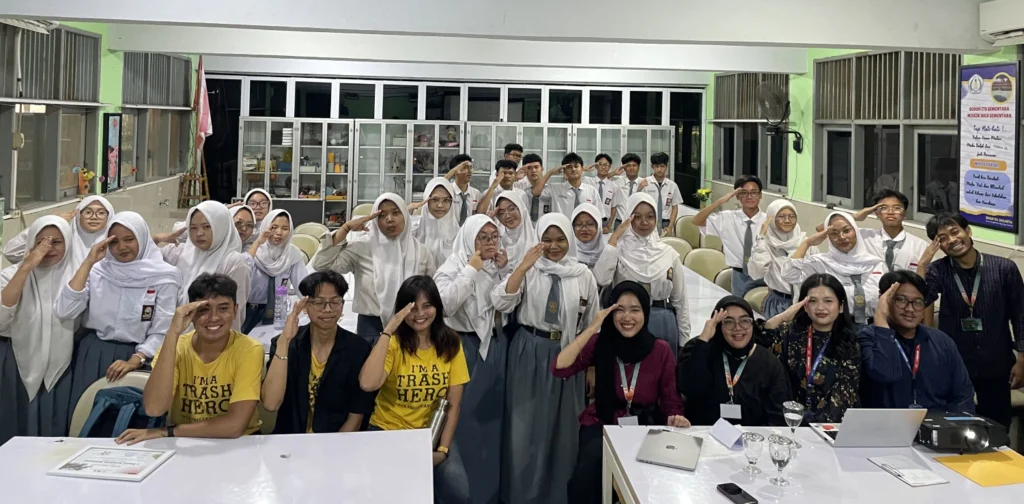 sekumpulan anak berseragam SMA dan delapan orang berbaju bebas berpose menghadap kamera di dalam ruang kelas