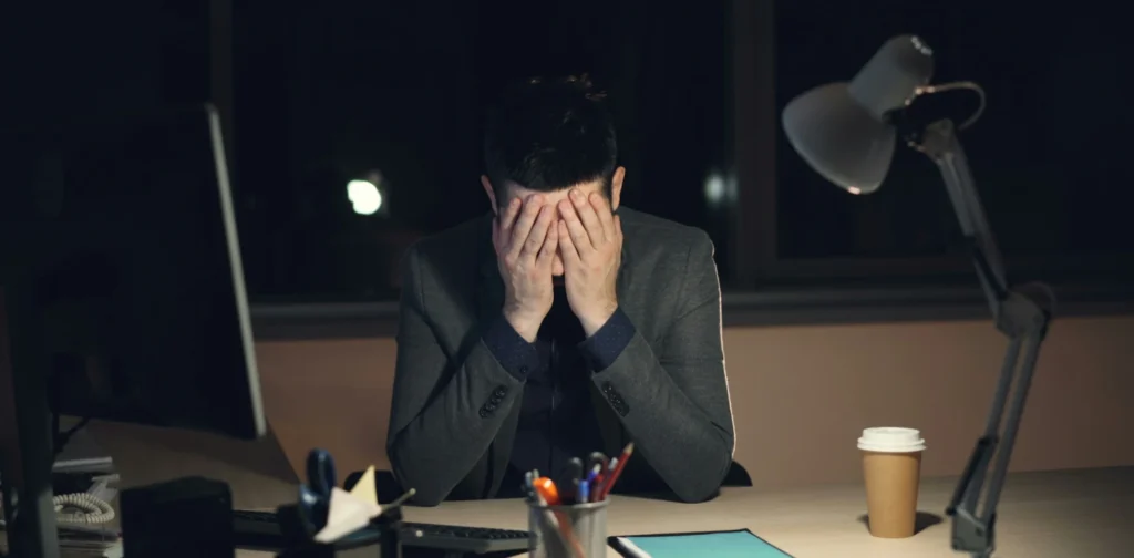 Seorang pemuda yang tampak lelah menutup wajah dengan kedua tangan duduk di depan komputer