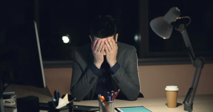 Seorang pemuda yang tampak lelah menutup wajah dengan kedua tangan duduk di depan komputer