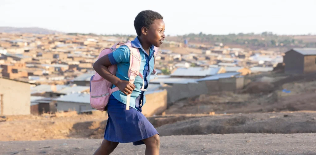 seorang anak berseragam sekolah dengan ransel berjalan mendaki bukit