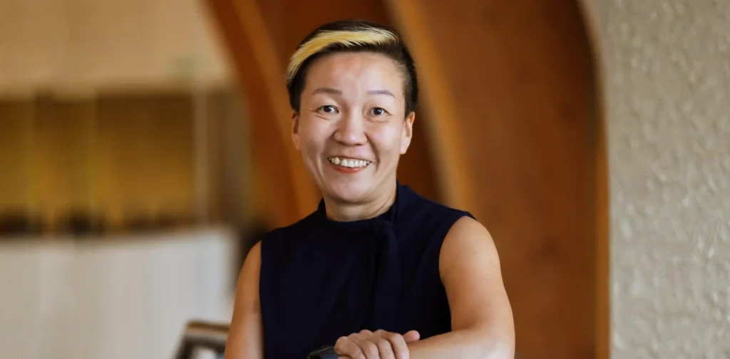 May Tan-Mullis, seorang perempuan berambut pendek mengenakan blus hitam tanpa lengan tersenyum ke arah kamera.