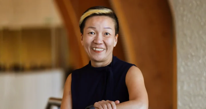 May Tan-Mullis, seorang perempuan berambut pendek mengenakan blus hitam tanpa lengan tersenyum ke arah kamera.