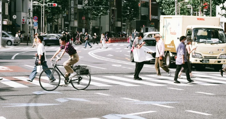 orang-orang menyeberang jalan lewat zebra cross dan seorang di antaranya dengan sepeda