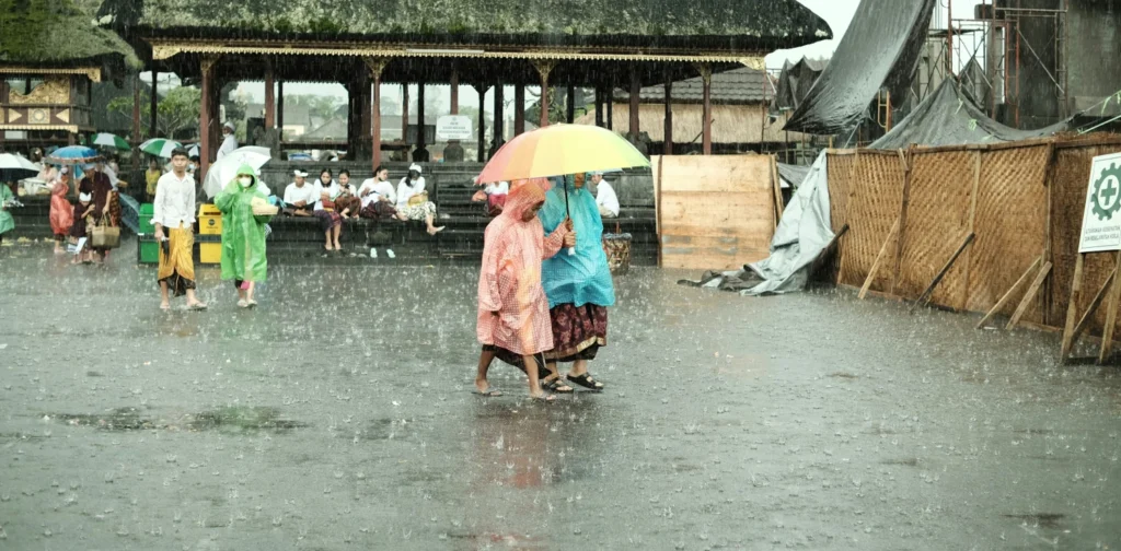 orang-orang mengenakan jas hujan dan memegang payung berjalan di tengah hujan