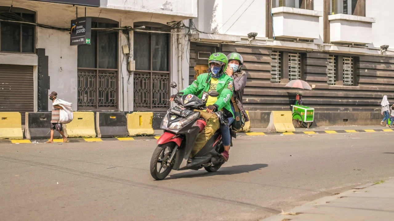 dua orang berkendara dengan sepeda motor.
