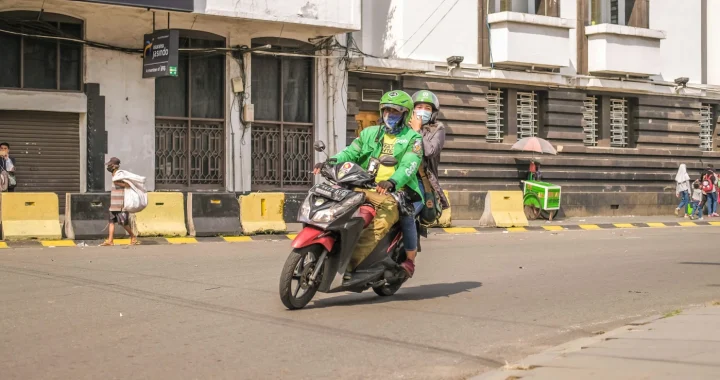 dua orang berkendara dengan sepeda motor.