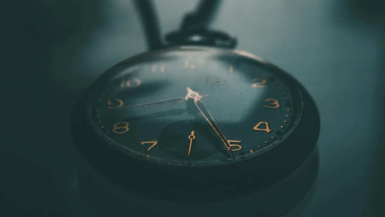 sebuah jam kantong berwarna hitam dengan angka berwarna emas di atas meja