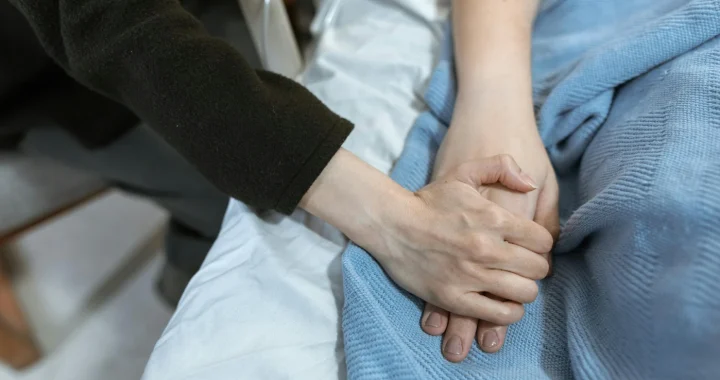 sebuah tangan dengan baju hitam memegang tangan lainnya di atas kain biru