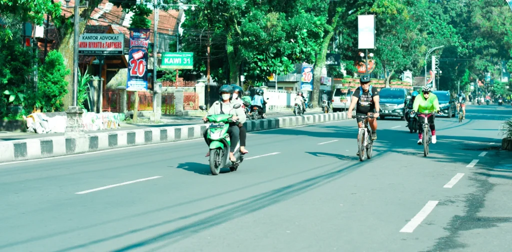 beberapa orang berkendara dengan motor dan sepeda di jalan yang lengang.
