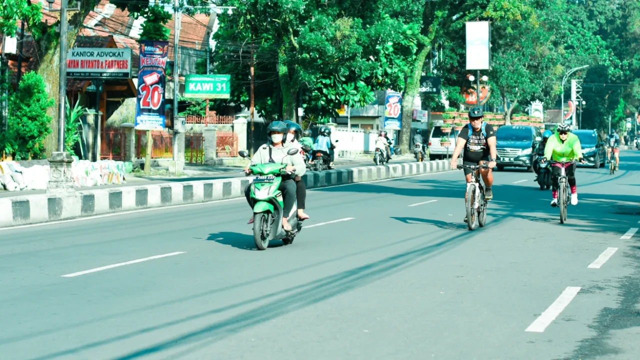 beberapa orang berkendara dengan motor dan sepeda di jalan yang lengang.