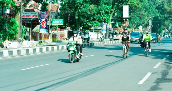 beberapa orang berkendara dengan motor dan sepeda di jalan yang lengang.