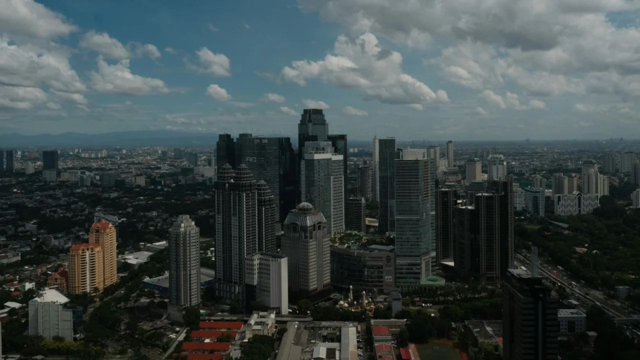 hamparan permukiman dengan gedung-gedung pencakar langit dengan langit biru dan taburan awan putih.