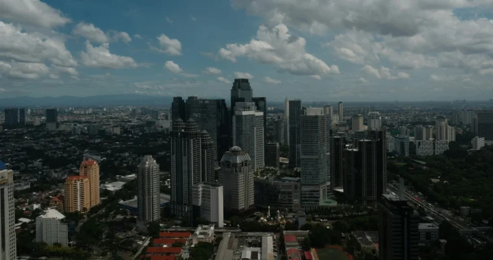 hamparan permukiman dengan gedung-gedung pencakar langit dengan langit biru dan taburan awan putih.