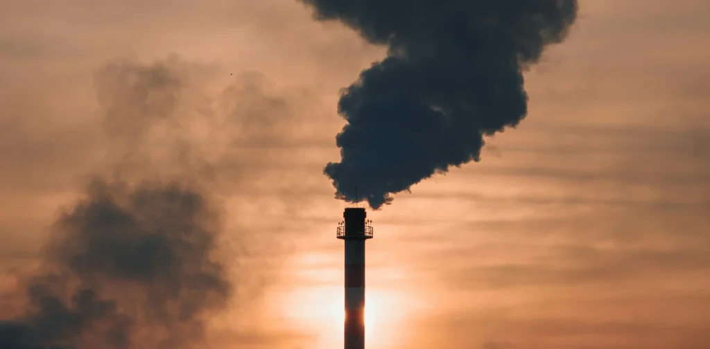 asap hitam dari cerobong pabrik membumbung ke langit jingga