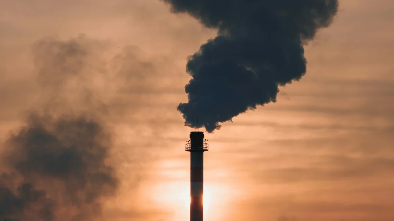 asap hitam dari cerobong pabrik membumbung ke langit jingga