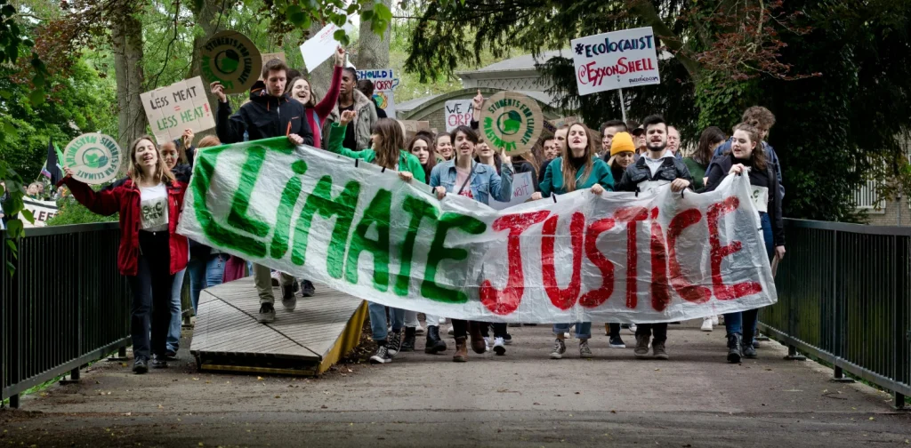 Sekelompok aktivis muda berbaris melintasi jembatan sambil membawa spanduk besar bertuliskan “Climate Justice” dan tanda-tanda protes selama aksi mogok iklim