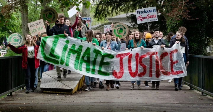 Sekelompok aktivis muda berbaris melintasi jembatan sambil membawa spanduk besar bertuliskan “Climate Justice” dan tanda-tanda protes selama aksi mogok iklim