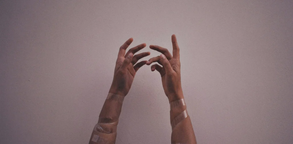 tangan seseorang dengan plaster terangkat ke atas dengan latar abu-abu