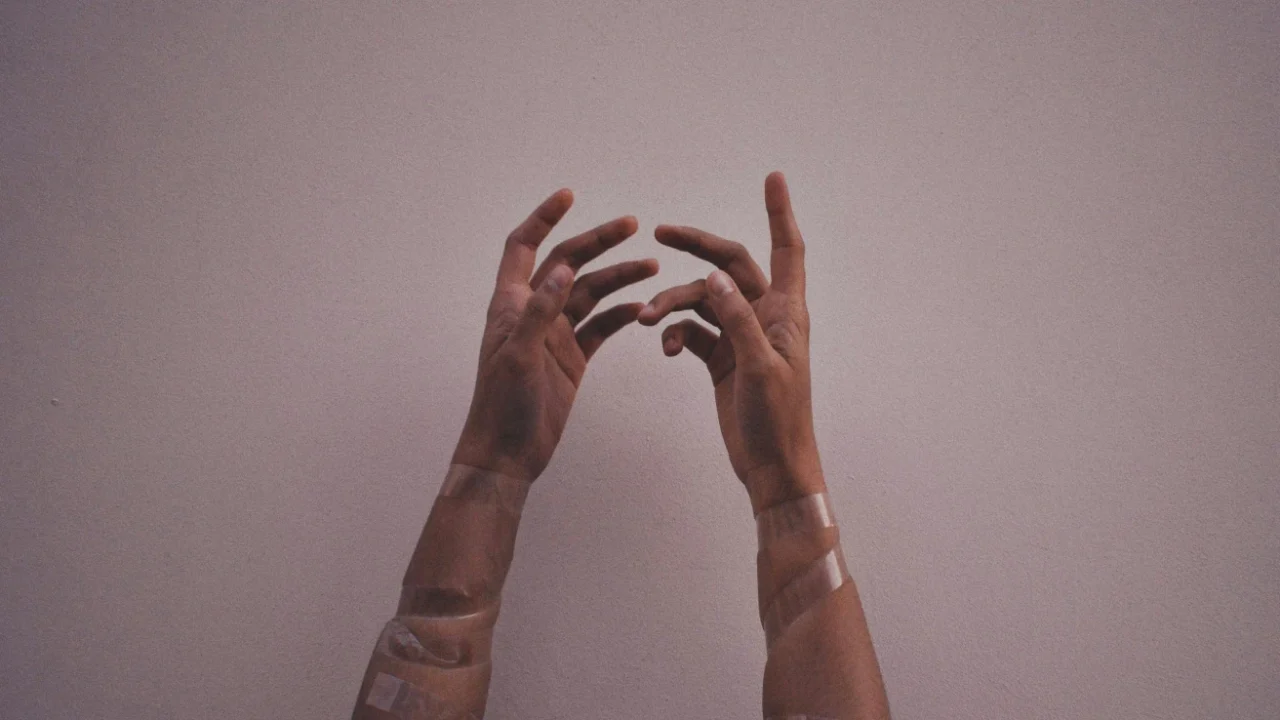 tangan seseorang dengan plaster terangkat ke atas dengan latar abu-abu