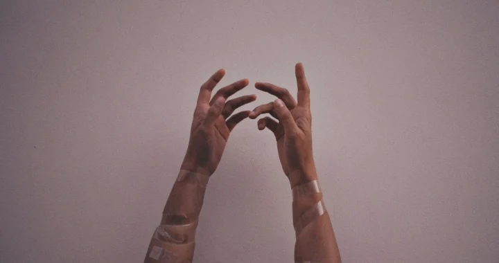 tangan seseorang dengan plaster terangkat ke atas dengan latar abu-abu