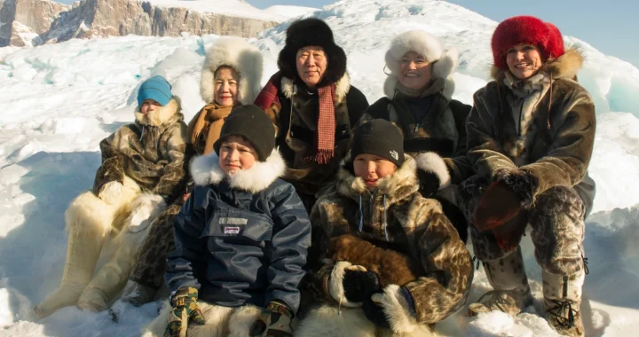 Ban Ki-moon bersama orang-orang Inuit yang mengenakan jaket tebal di atas salju.