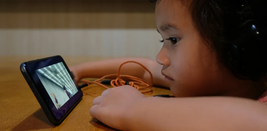 seorang anak dengan headset menatap layar ponsel