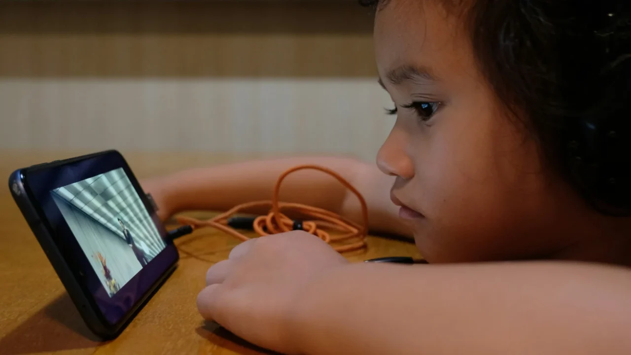 seorang anak dengan headset menatap layar ponsel