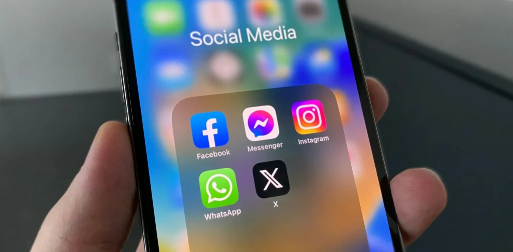 sebuah tangan memegang ponsel pintar dengan layar menampilkan icon media sosial