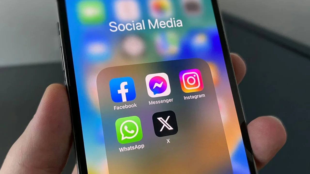 sebuah tangan memegang ponsel pintar dengan layar menampilkan icon media sosial