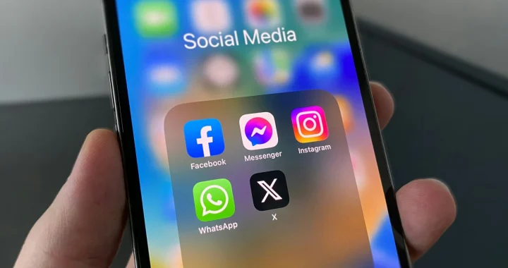 sebuah tangan memegang ponsel pintar dengan layar menampilkan icon media sosial