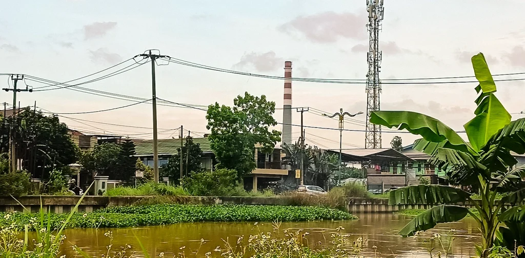 badan air berwarna kecoklatan dengan latar bangunan dan corong pabrik