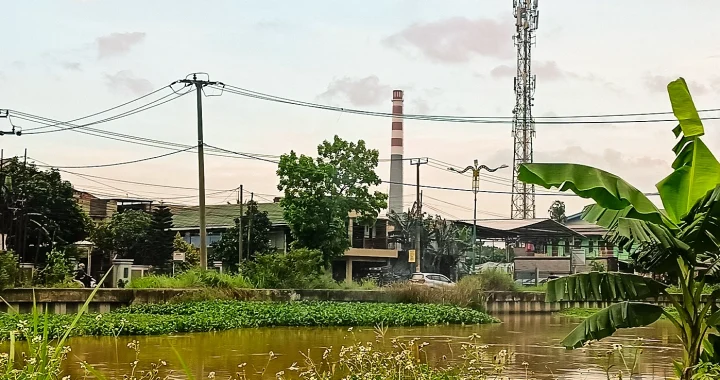 badan air berwarna kecoklatan dengan latar bangunan dan corong pabrik