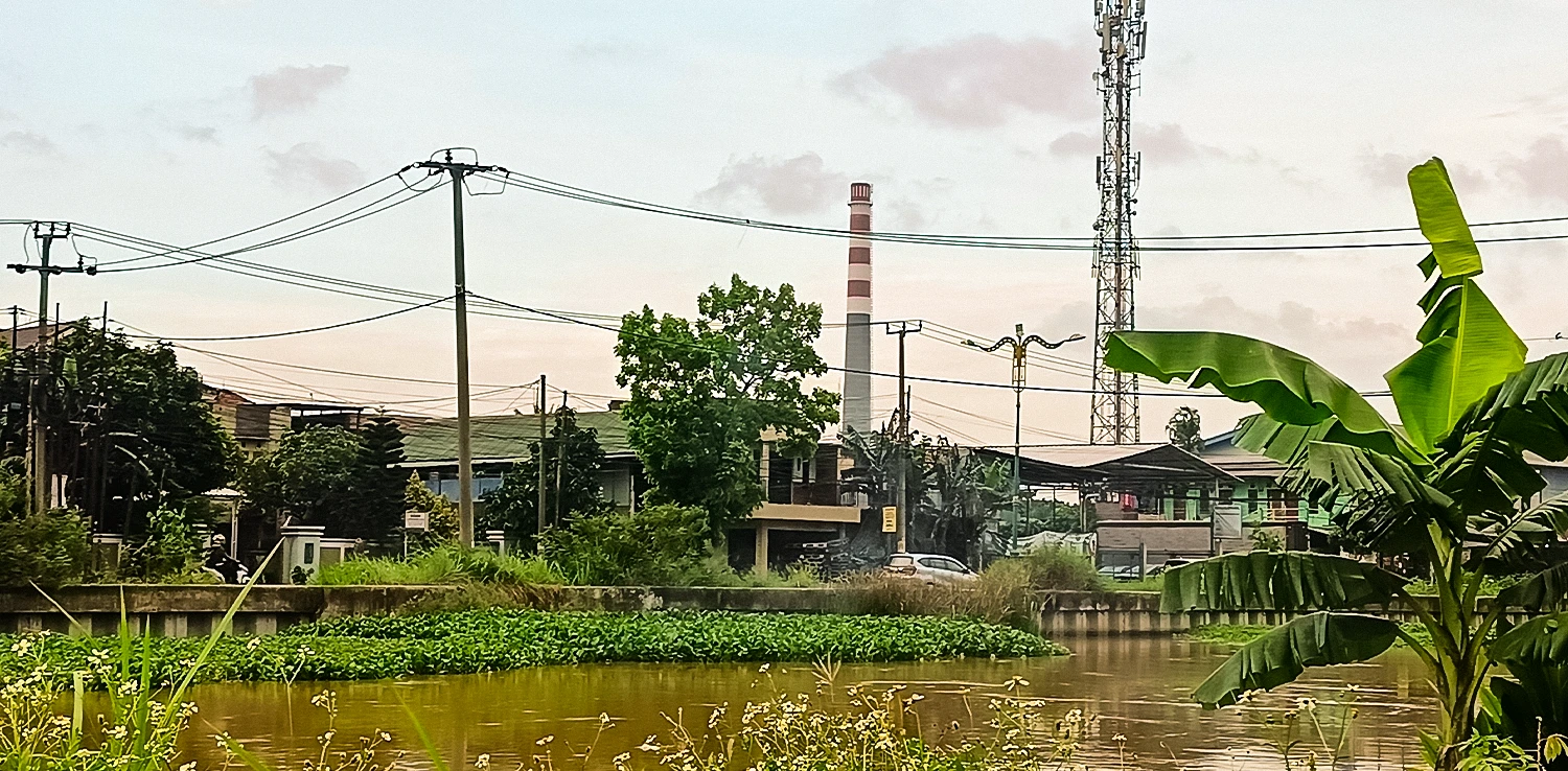 badan air berwarna kecoklatan dengan latar bangunan dan corong pabrik