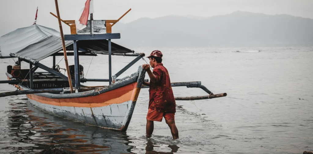 seorang nelayan berbaju merah mendorong perahu ke badan air