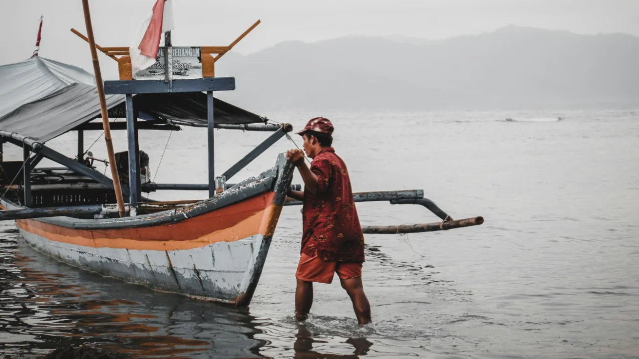 seorang nelayan berbaju merah mendorong perahu ke badan air