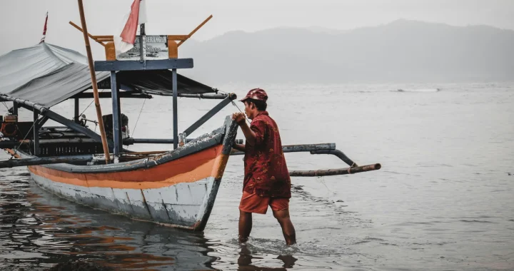 seorang nelayan berbaju merah mendorong perahu ke badan air