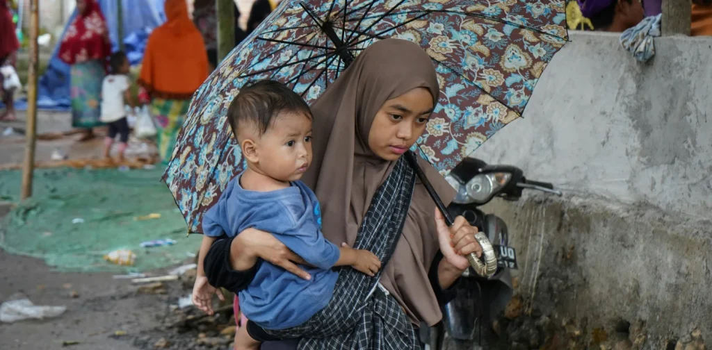 seorang anak digendong oleh seorang perempuan di bawah payung