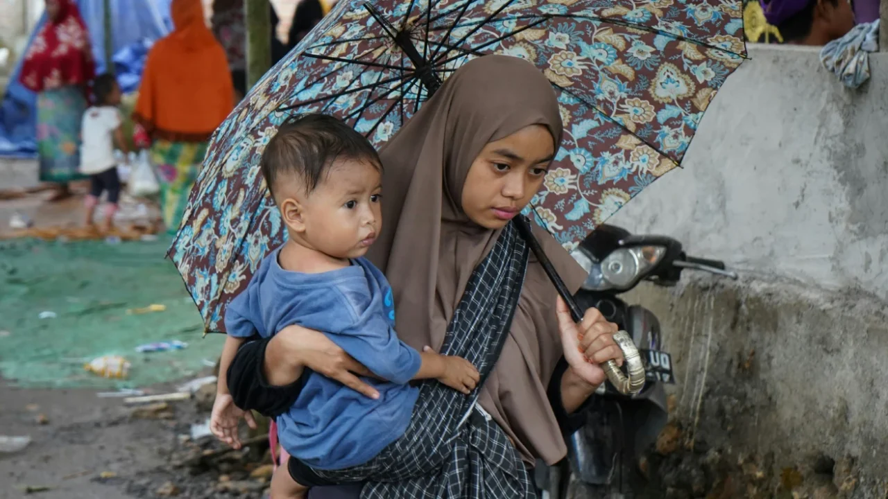 seorang anak digendong oleh seorang perempuan di bawah payung