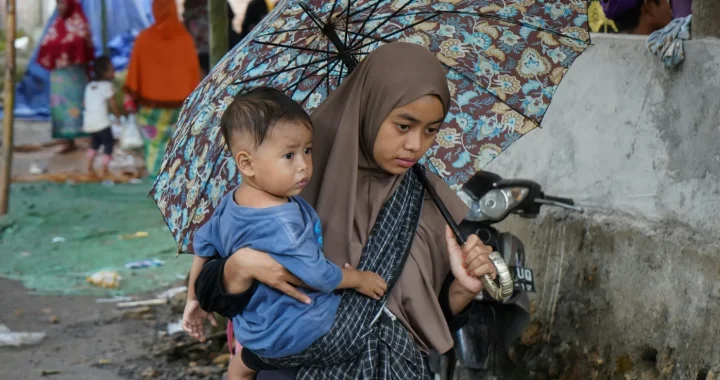 seorang anak digendong oleh seorang perempuan di bawah payung