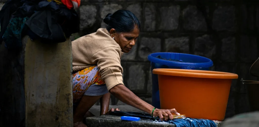 seorang perempuan menyikat pakaian di atas lempengan batu di lantai